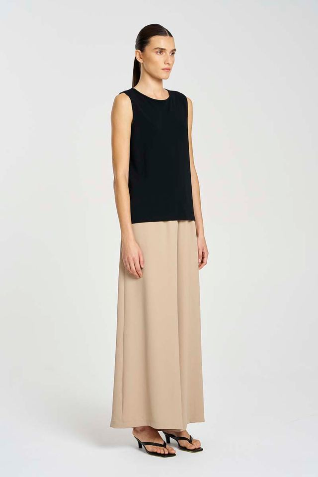 Woman wearing a black sleeveless top and beige wide-leg pants on a white background