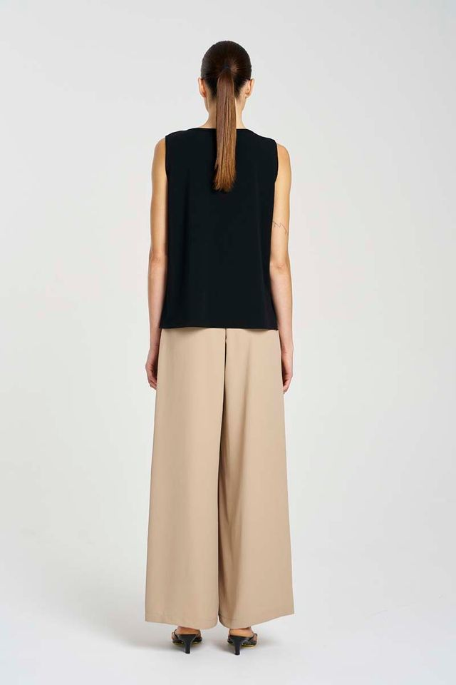 Person wearing a black sleeveless top and beige wide-leg pants on a white background