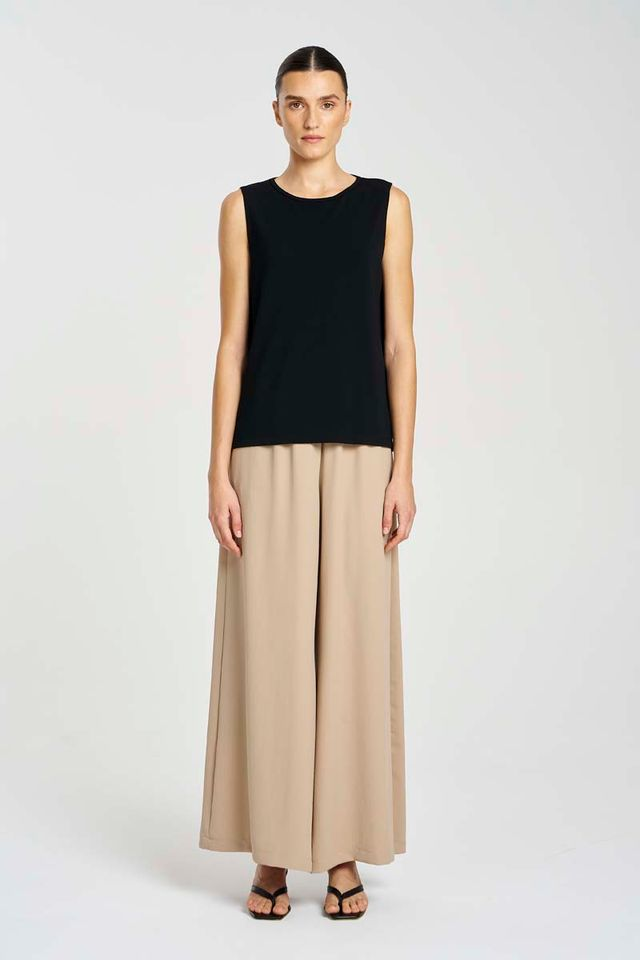 Woman wearing a black sleeveless top and beige wide-leg pants on a white background