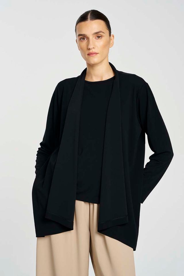 Person wearing a black cardigan over a black top with beige pants on a white background