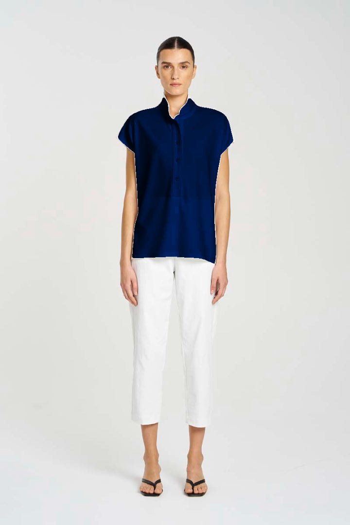 Woman wearing a navy sleeveless top and white pants on a white background