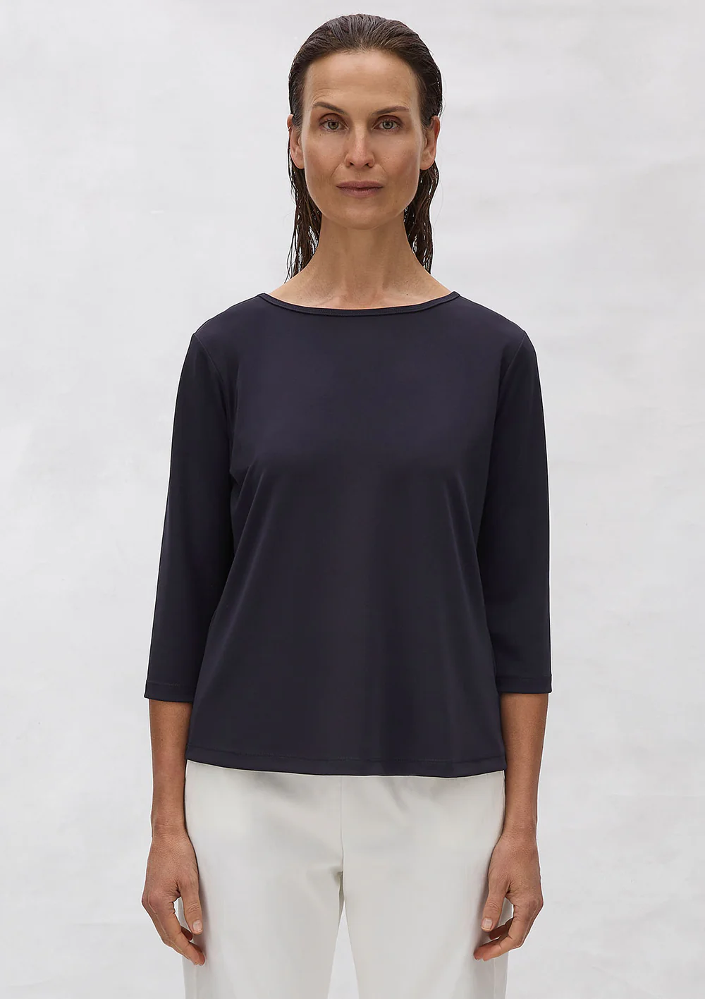 Woman wearing a black top and white pants against a plain background