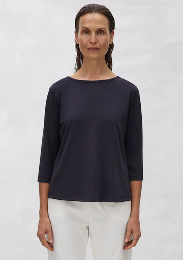 Woman wearing a black top and white pants against a plain background