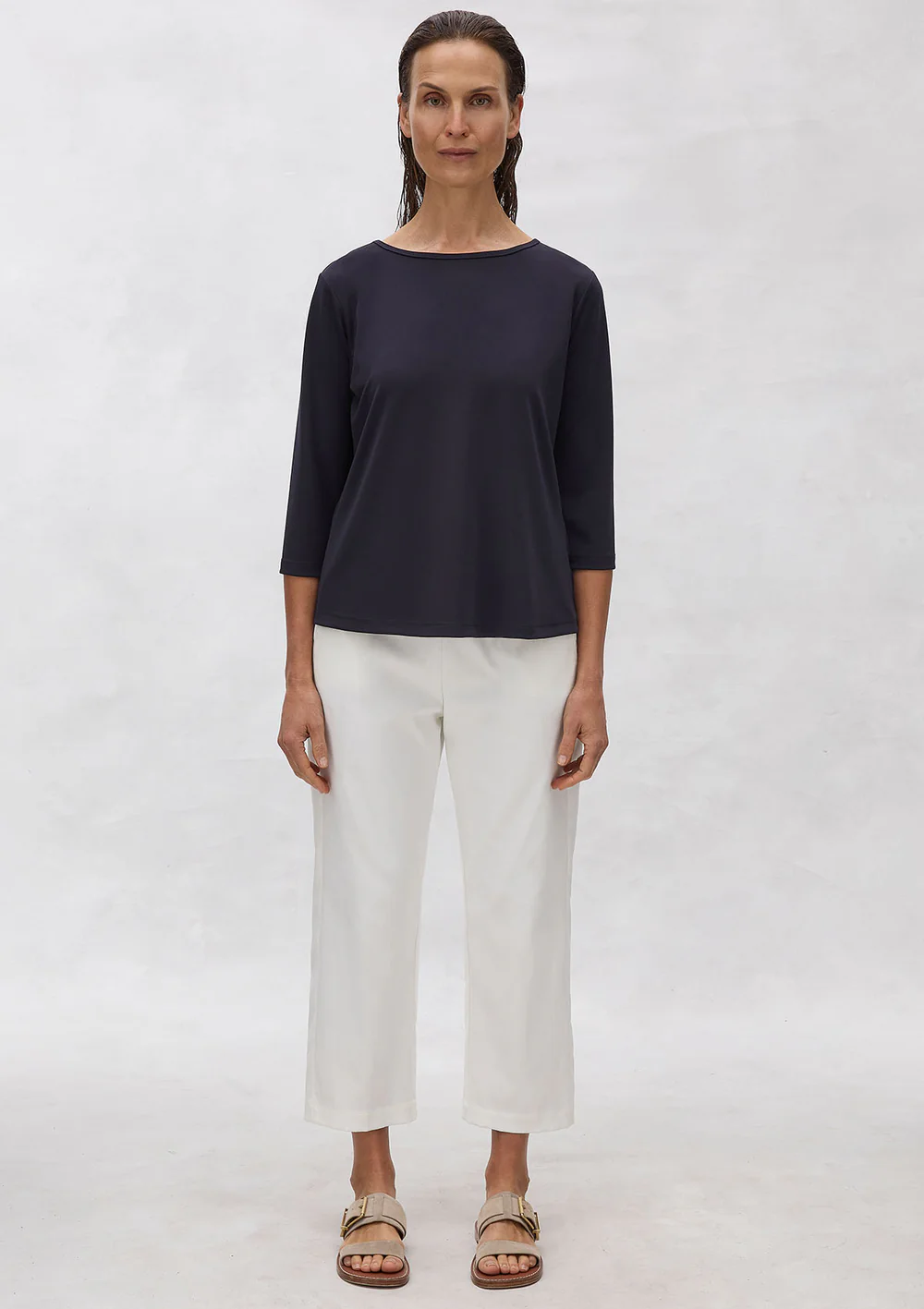 Woman wearing a navy top and white pants on a plain background