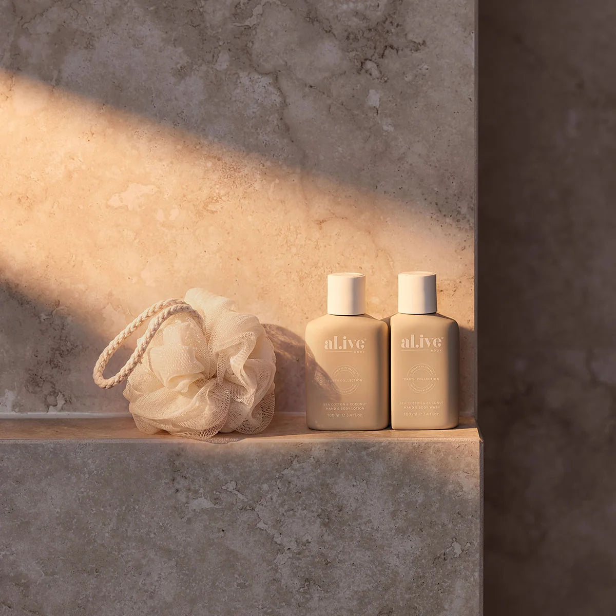 al.ive body Sea Cotton & Coconut travel bottles and loofah on a stone ledge