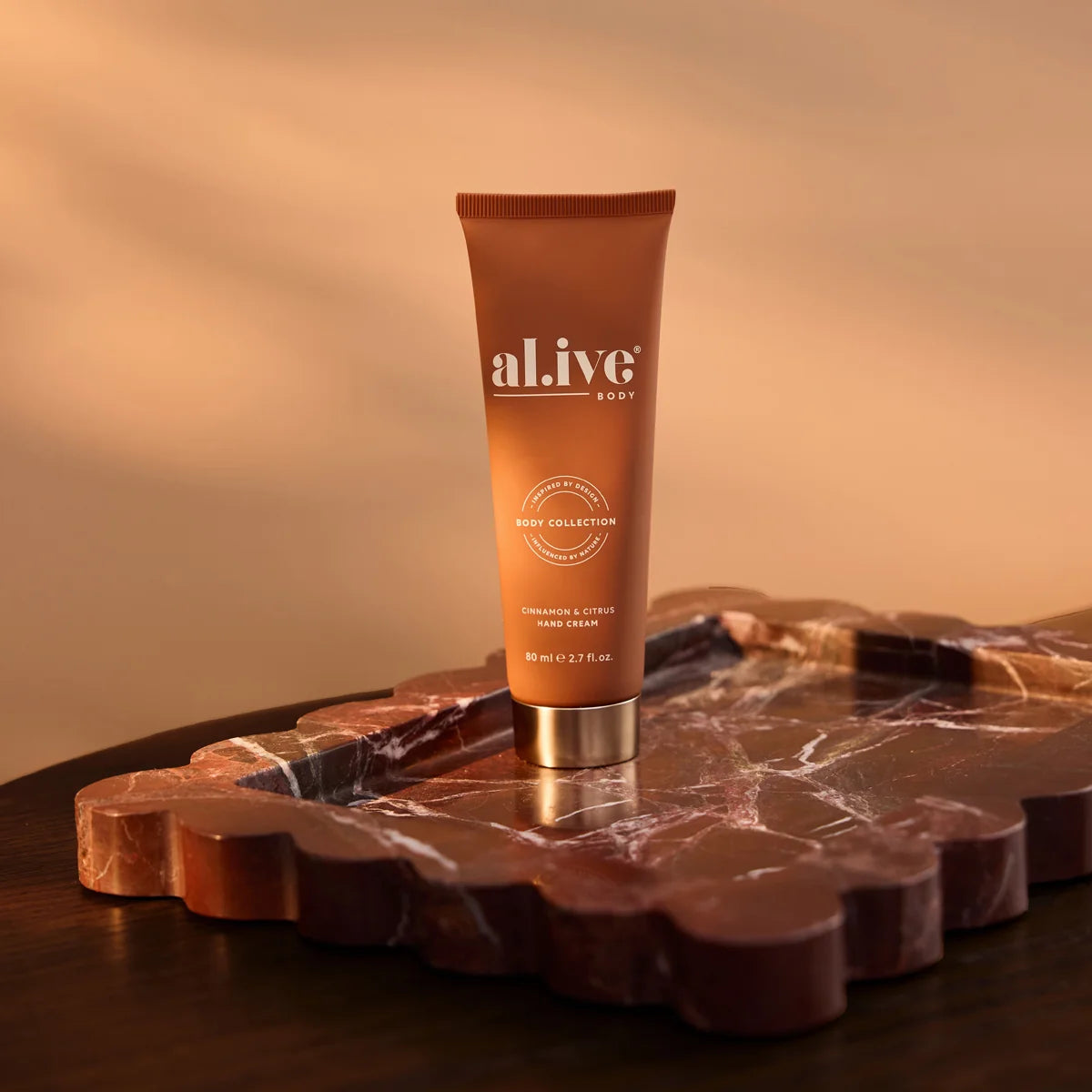 al.ive body Cinnamon & Citrus Hand Cream on a marble tray in warm light