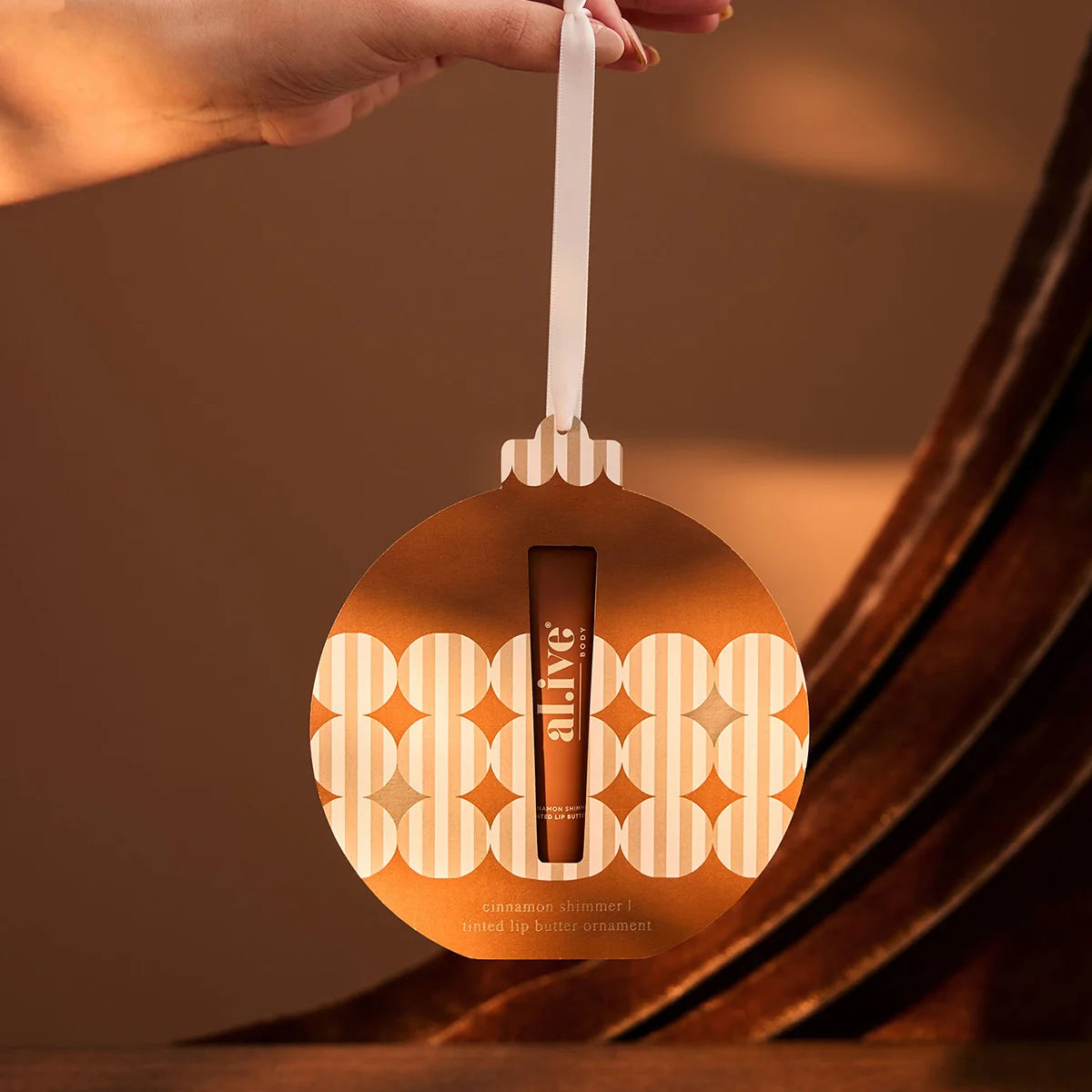 al.ive body Tinted Lip Butter Ornament hanging from its ribbon