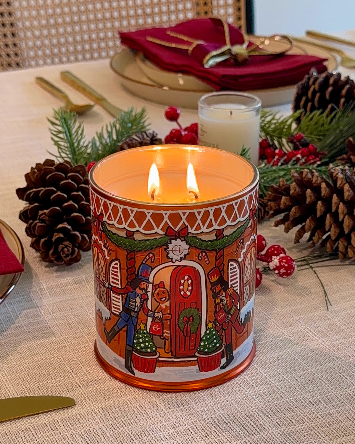 Glasshouse Fragrances Gingerbread House Candle glowing on a Christmas table with pine cones